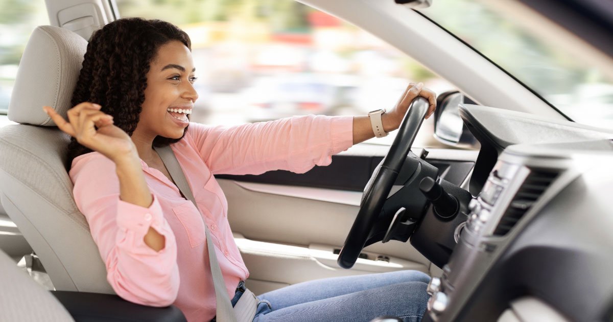African American woman wearing pink shirt and jeans happily driving her luxury sedan