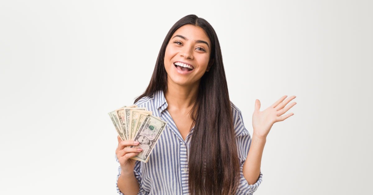 Photo of South American woman with long black hair wearing striped button down shirt and holding stack of cash in her right hand with grey backdrop
