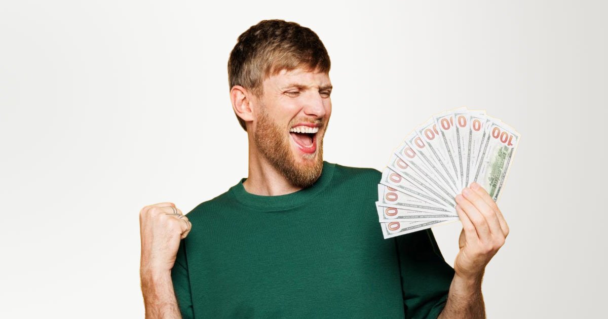 White man in his 20s holding a fanned out stack of $100s wearing a green shirt with a yellow background