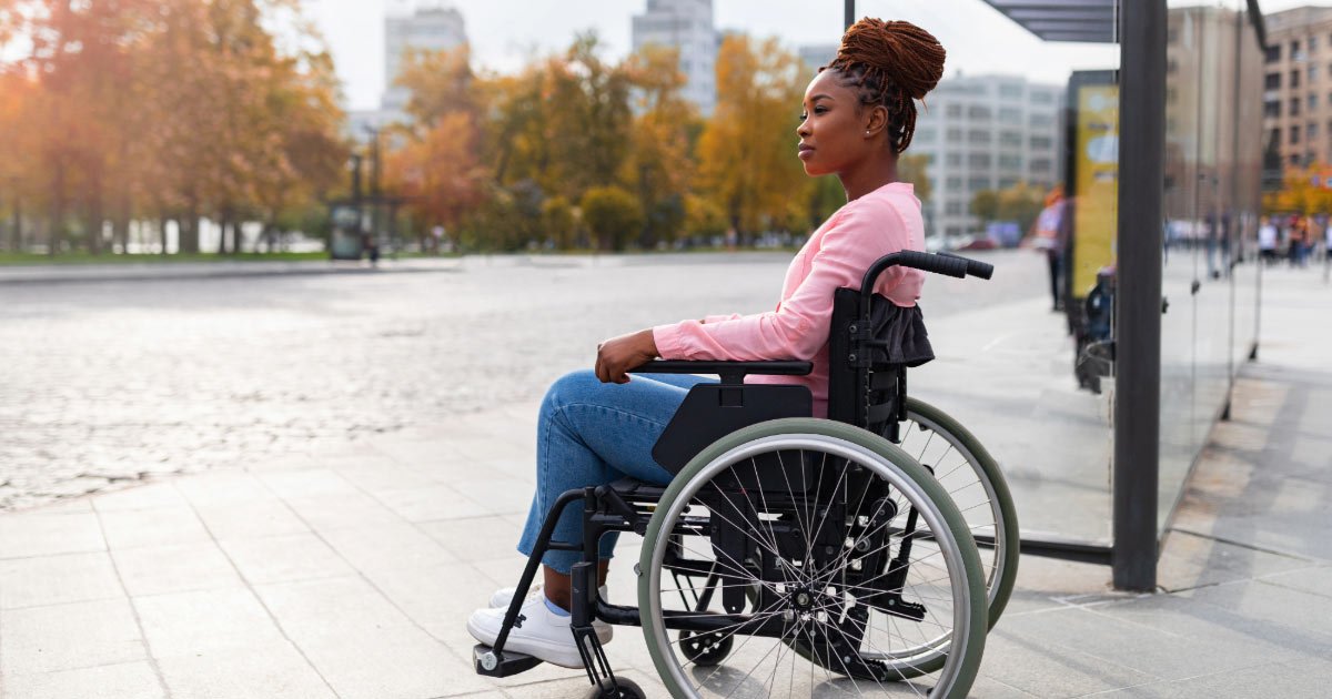 African American woman sitting in wheelchair waiting at bus stop