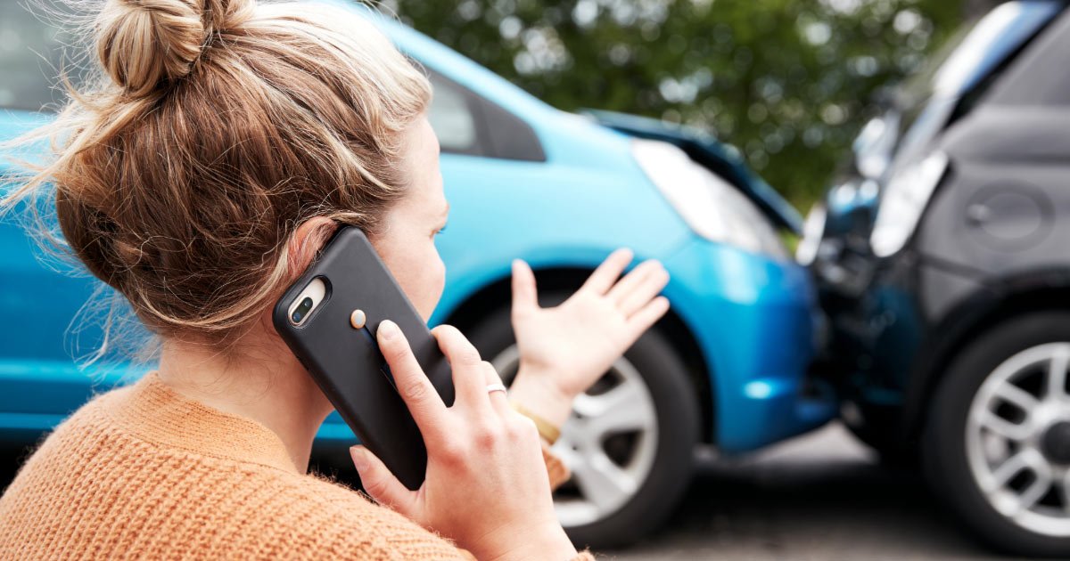 Woman on her mobile phone looking at her car after a rear-end accident