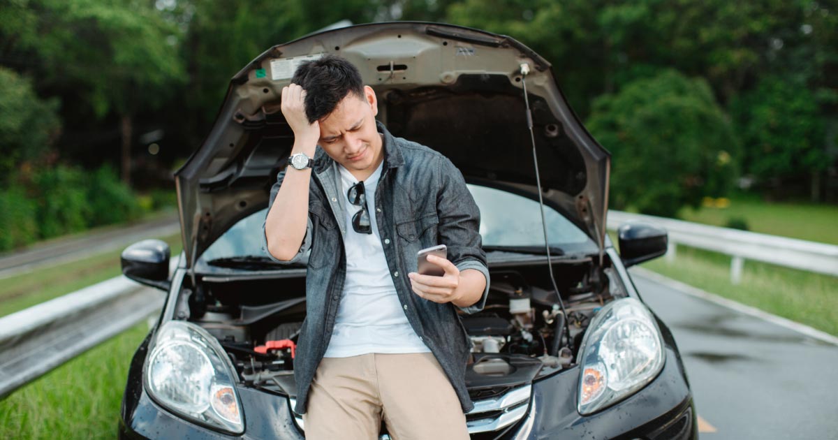 Man leaning on front of his broken down car with hood up