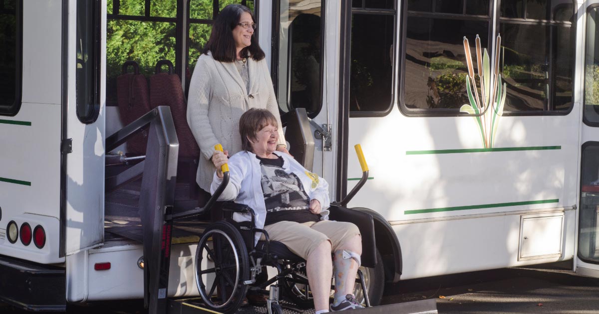 Elderly woman in wheelchair being assisted off of bus ramp