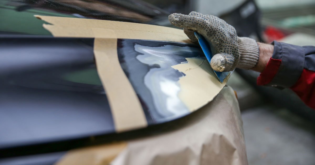 Automotive repair mechanic doing body panel work on a damaged car