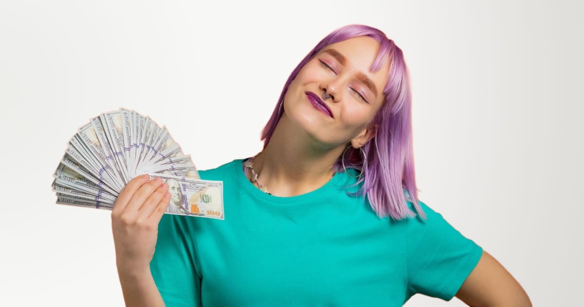 White girl with purple hair and lipstick fanning out 100 dollar bills wearing teal shirt standing in front of orange background