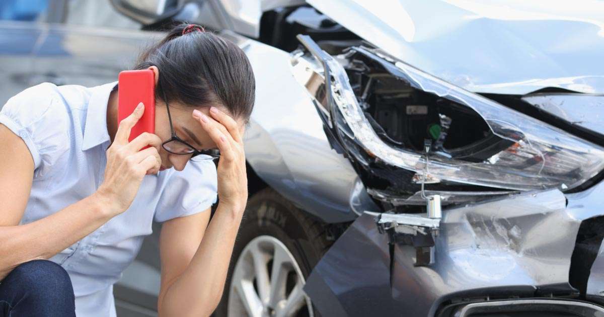 Woman on mobile phone hunched down next to her wrecked Nissan