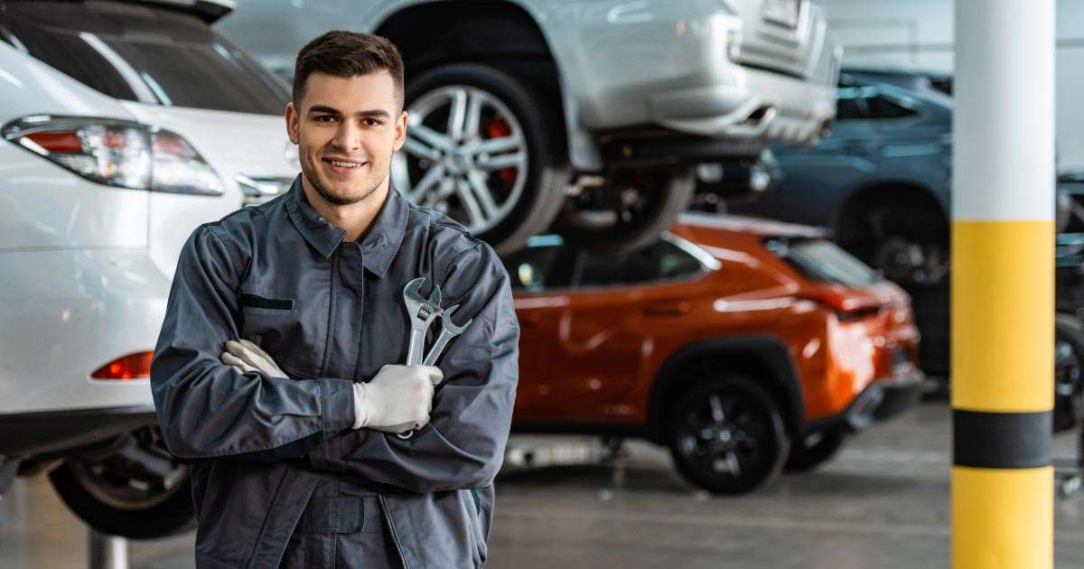 Nissan mechanic standing in front of cars on lifts holding two wrenches