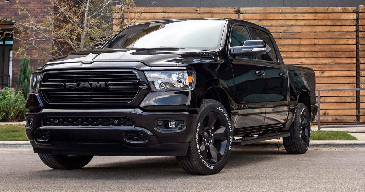 Black 2-door Dodge Ram pickup truck with black wheels parked in front of a wooden garage in a yard