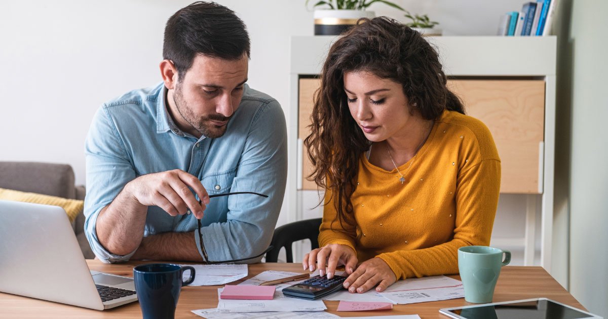 Husband and wife sitting a kitchen table with calculator assessing their monthly bills and car costs